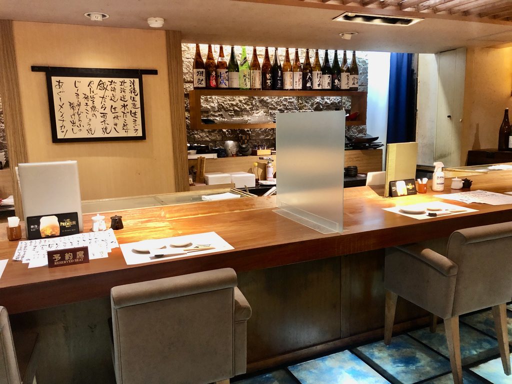 海鮮魚じんの店内、日本酒の瓶が並ぶカウンター